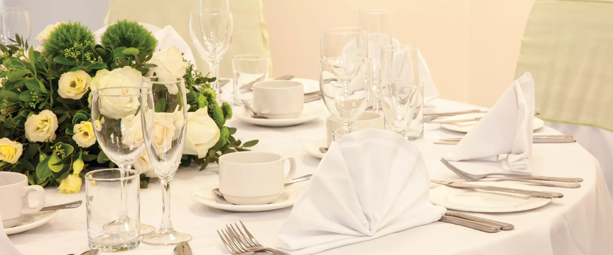 A table set up for a wedding breakfast with a white table cloth, floral centrepiece and a full dining set.