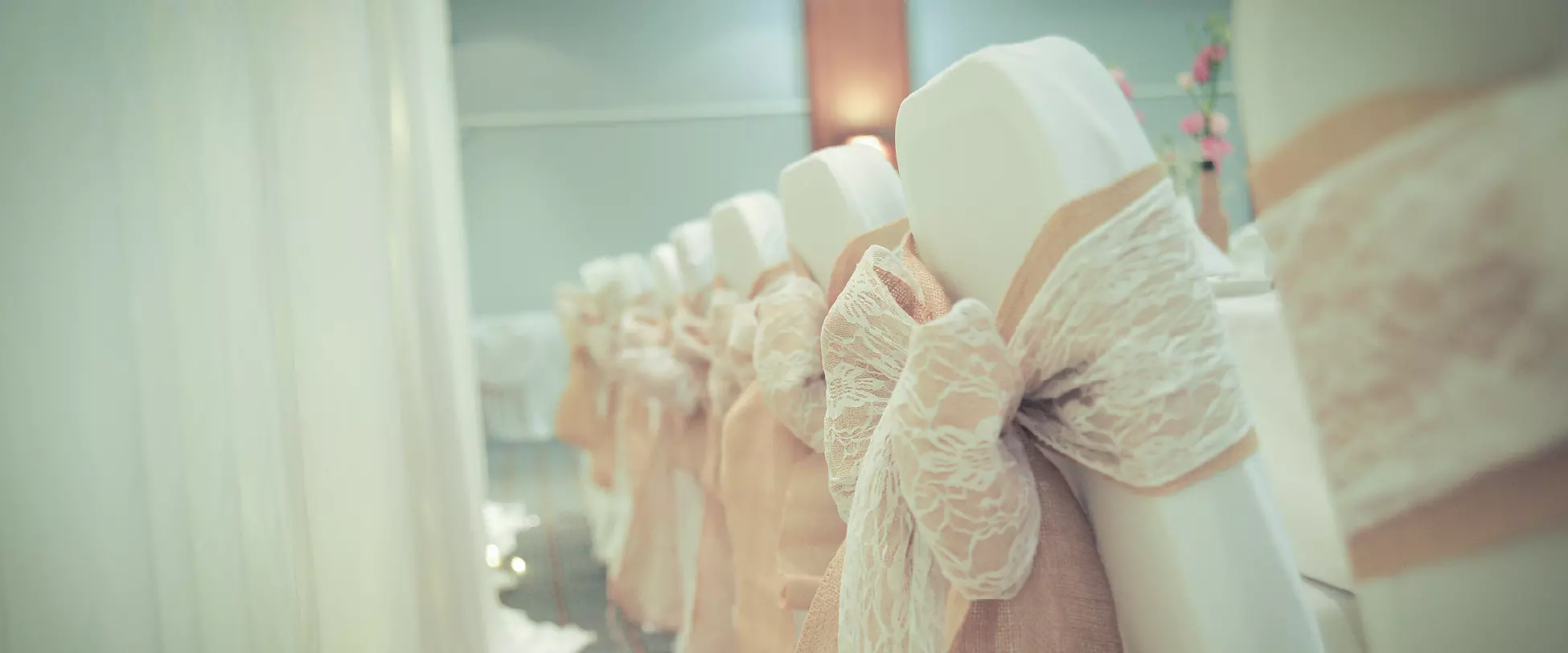 Chairs set up for the bridal party at a wedding breakfast. The chairs are covered in white and have pink ribbons.